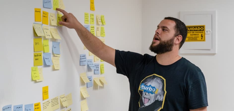 Homem de pé escrevendo em post it na parede com foco em anotações mais próximas.