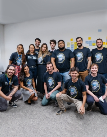 Grupo de pessoas de negócios concentradas no meio de uma sala com post its na parede durante dinâmica de grupo.