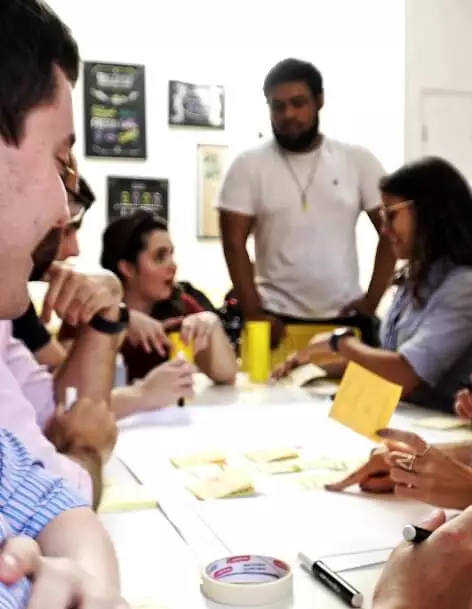 Grupo de pessoas felizes conversando e escrevendo em post its durante uma dinâmica de grupo.